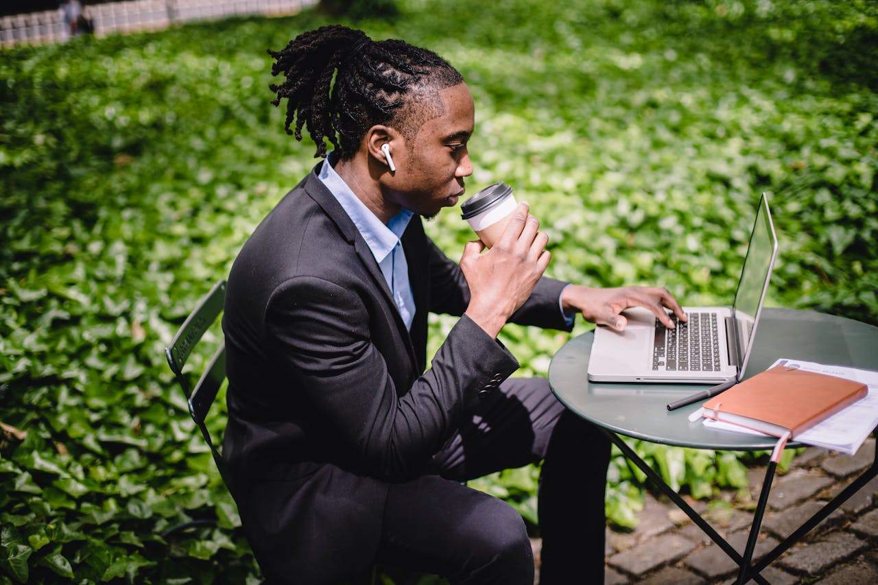 A man wearing earbuds working on a computer in a park